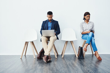 Poster - Quickly doing final preparations before the big presentation. Full length shot of two young businesspeople sitting down on chairs and using their tech devices against a grey background.