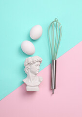 Wall Mural - Culinary minimal flat lay still life. Bust of David, eggs and whisk on a blue-pink pastel background. Top view