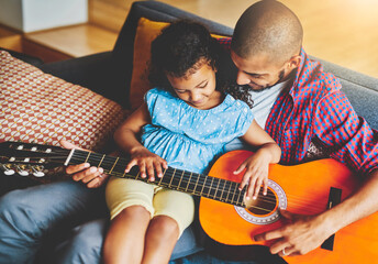 Sticker - To share music is to share love. Shot of an adorable little girl and her father playing a guitar together on the sofa at home.