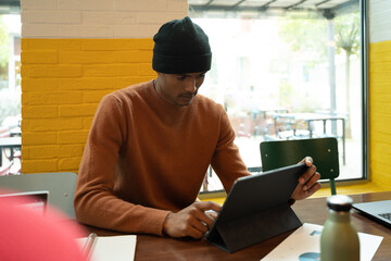 Young focused man in casual wear works in a co-working space uses digital touchpad