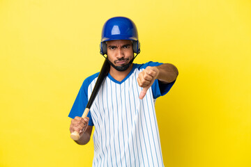 Wall Mural - Young Colombian latin man playing baseball isolated on yellow background showing thumb down with negative expression