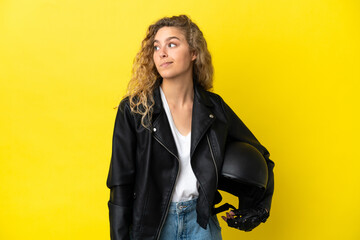 Wall Mural - Young blonde woman with a motorcycle helmet isolated on yellow background looking to the side