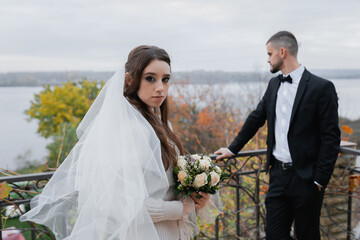 Wall Mural - Young cheerful wedding couple. A bride with a veil, a charming groom in a black suit.