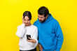 © luismolinero - Young caucasian couple isolated on yellow background reading a message with the mobile