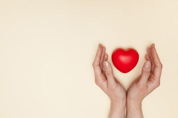 Health, medicine and charity concept - close up of female hands with small red heart