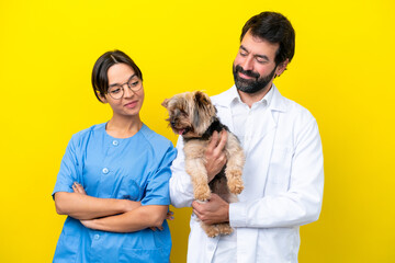 Young veterinarian couple with dog isolated on yellow background with happy expression