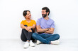 © luismolinero - Young caucasian couple sitting on the floor isolated on white background looking at each other