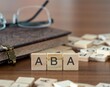 the acronym aba for merican bankers or bar association word or concept represented by wooden letter tiles on a wooden table with glasses and a book