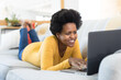© Wavebreak Media - Smiling mid adult african american woman using laptop while lying on sofa at home