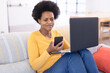 © Wavebreak Media - Smiling mid adult african american female freelancer using smart phone and laptop on sofa