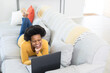 © Wavebreak Media - Happy mid adult african american woman using laptop while lying on sofa at home