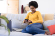 © Wavebreak Media - Smiling mid adult african american female freelancer using phone while sitting with laptop on sofa