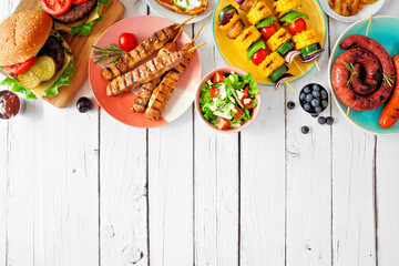 Wall Mural - Summer BBQ or picnic food top border. Variety of burgers, grilled meat, vegetables, fruits, salad and potatoes. Overhead view on a white wood background. Copy space.