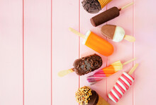 Mixture of chocolate and colorful summer popsicles and ice cream treats. Top down view side border on a pink wood background. Copy space.
