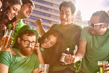 Group Of Friends Gathered Around One Man Who Is Refusing To Have Fun At St Patrick's Day Party