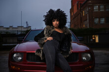 Young African American Woman With Hands On Hips Leaning On Car Looking Into Camera With Attitude
