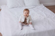 © Tatyana - Sweet  little 1-year-old daughter sitting on chair in grey dress.Portrait of Girl baby child on bed at home. Tenderness and love, sweetness. Lovely family indoors.Serious baby portrait indoors