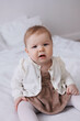 © Tatyana - Sweet  little 1-year-old daughter sitting in bed in beige dress.Portrait of Girl baby child at home. Tenderness and love, sweetness. Lovely family indoors.Serious baby portrait indoors