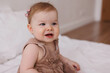 © Tatyana - Sweet  little 1-year-old daughter sitting on chair in grey dress.Portrait of Girl baby child on bed at home. Tenderness and love, sweetness. Lovely family indoors.Serious baby portrait indoors