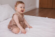 © Tatyana - Sweet  little 1-year-old daughter sitting on chair in grey dress.Portrait of Girl baby child on bed at home. Tenderness and love, sweetness. Lovely family indoors.Serious baby portrait indoors