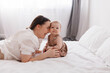 © Tatyana - Sweet young mother playing with her little 1-year-old daughter in bed.Caring brunette woman laying with her baby child at home. Tenderness and love between mother and daughter. Lovely family indoors.