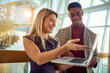 © luckybusiness - A young business woman is showing a laptop content to a male colleague while standing in the hallway. Business, people, company