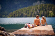 © luckybusiness - A young couple is taking a sunbath on the dock at the lake during mountain hiking. Trip, nature, hiking