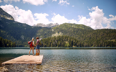 Wall Mural - A young couple is standing on the dock at the lake and enjoying the view during mountain hiking. Trip, nature, hiking