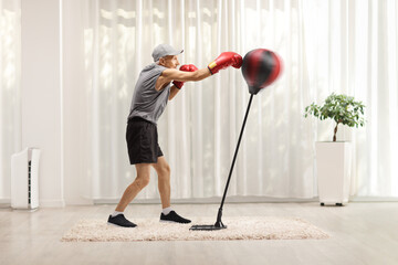 Wall Mural - Full length profile shot of an elderly man with punching a free stnading boxing bag