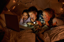 Kids Are Never Far From Technology. Shot Of Three Young Children Using A Laptop In A Blanket Fort.