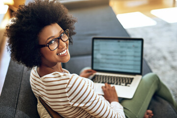 No better way to work than to work from home. Portrait of a cheerful young woman working on her laptop while being seated comfortably on a couch at home.