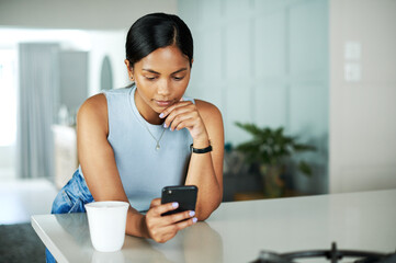 Poster - Hmm, this looks just about right. Shot of an attractive young woman leaning on her kitchen counter and looking contemplative while using her cellphone.