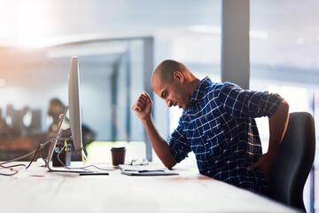 Poster - Feeling the strain that poor posture places on the back. Cropped shot of a young designer experiencing back pain while working at his desk.