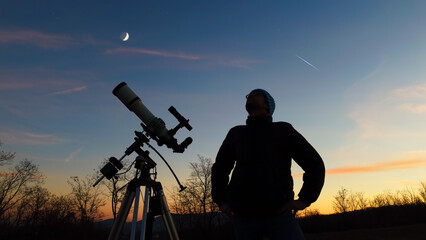 Wall Mural - silhouette of a man, telescope and countryside under evening skies.