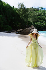 Wall Mural - Beautiful young woman in long green dress and straw hat on Seychelles beach on Mahe or La Digue island