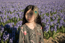 Asian Girl In Floral Dress In Field Of Purple Hyacinth Flowers Holding Peacock Feather