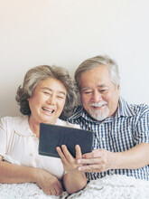 Senior Couple Using A Tablet Phone Computer Face Time Call To Relatives Descendant Relatives Grandchild, Smiling Feel Happy In Sofa At Home - Lifestyle Senior Concept