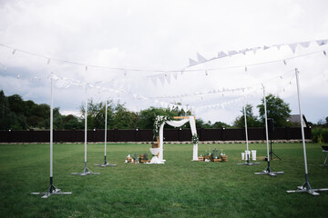 Wall Mural - Wooden arch for the wedding ceremony and chairs. The wedding arch is decorated with bright flowers and lights in the form of a garland with candles. Beautiful decoration of the wedding ceremony