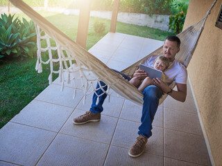 Wall Mural - Its their comfy spot to get connected. Shot of a father and his little daughter using a digital tablet while relaxing on a hammock outdoors.