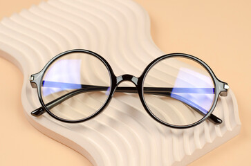 Poster - Stylish round glasses for vision on a wavy beige podium