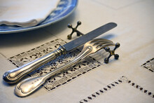 Antique Cutlery Made Of Blackened Silver, A Knife And Fork Lie On A Decorative Holder For Cutlery On An Embroidered Tablecloth Of The Dining Table.