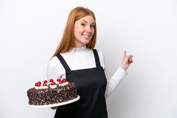 Wall Mural - Young redhead woman holding birthday cake isolated on white background pointing back