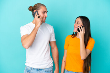 Wall Mural - Young caucasian couple isolated on blue background talking to mobile