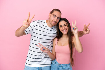 Wall Mural - Young caucasian couple isolated on pink background smiling and showing victory sign