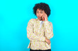 © Roquillo - Sad young girl with afro hairstyle wearing floral shirt over blue background talking on smartphone. Communication concept.