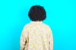 © Roquillo - The back view of a young girl with afro hairstyle wearing floral shirt over blue background . Studio Shoot.