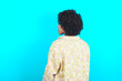 © Roquillo - The back side view of a young girl with afro hairstyle wearing floral shirt over blue background . Studio Shoot.