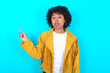 © Roquillo - Emotive Young woman with afro hairstyle wearing yellow fringe jacket keeps jaw dropped from shock demonstrates amazing promo points right on blank space demonstrates big shopping sale. Advertisement