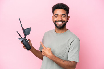 Brazilian man holding a drone remote control isolated on pink background and pointing it