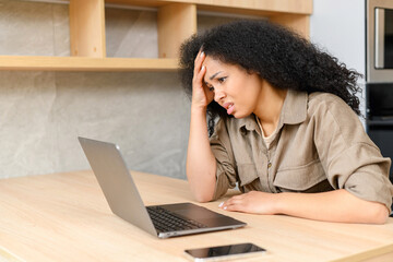 Bored female office employee sits at the desk in front of a laptop in the office, looks away and feels sad, a pensive young woman does not have inspiration for work, feels lack of sleep and fatigue